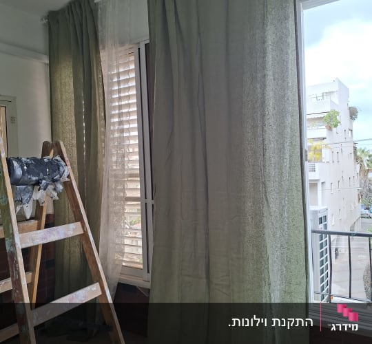 סולם ליד וילונות ירוקים בחדר עם חלון גדול